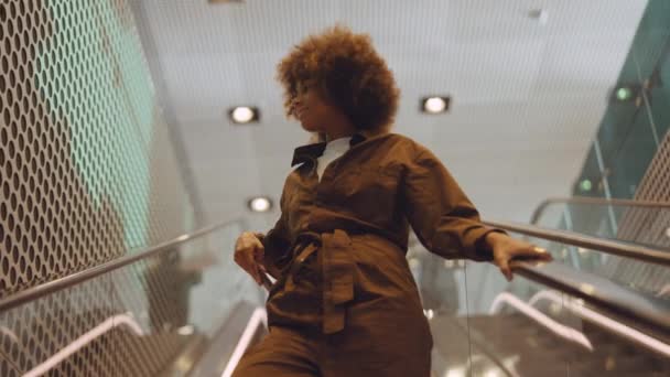 Женщина на эскалаторе улыбается смартфону, когда едет вниз — стоковое видео