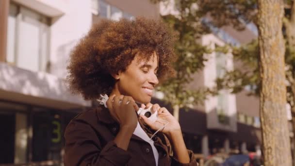 Женщина надевает наушники, чтобы слушать музыку в солнечном городе — стоковое видео