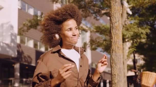 Женщина с афро в музыке из наушников в городе — стоковое видео