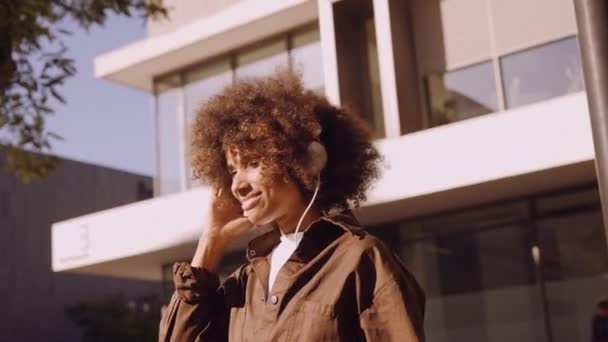 Vrouw met afro verloren in muziek van haar koptelefoon in de stad — Stockvideo