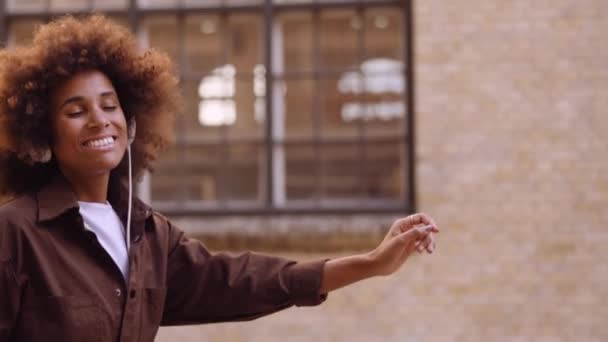 Mujer bailando con música a través de auriculares mientras se mueve por la calle — Vídeos de Stock