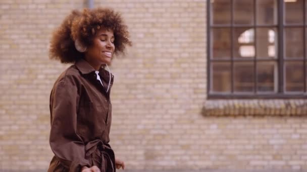 Kvinne danser til musikk gjennom hodetelefoner mens hun beveger seg nedover gaten – stockvideo