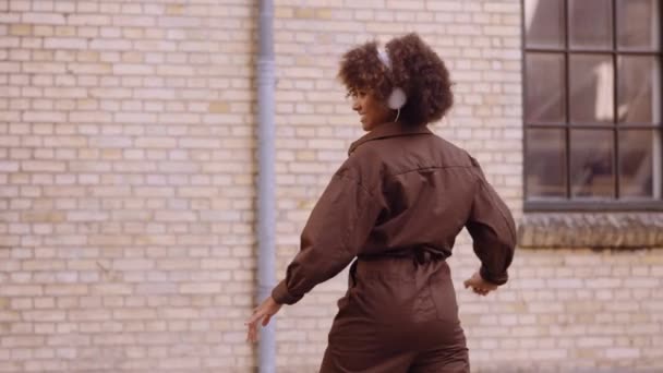 Dansande kvinna skrattar när hon lyssnar på musik genom hörlurar på gatan — Stockvideo