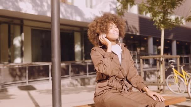 Vrouw verloren in muziek van koptelefoon op City Bench — Stockvideo