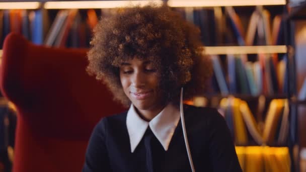 Mujer con cabello afro escuchando auriculares y sonriendo — Vídeo de stock