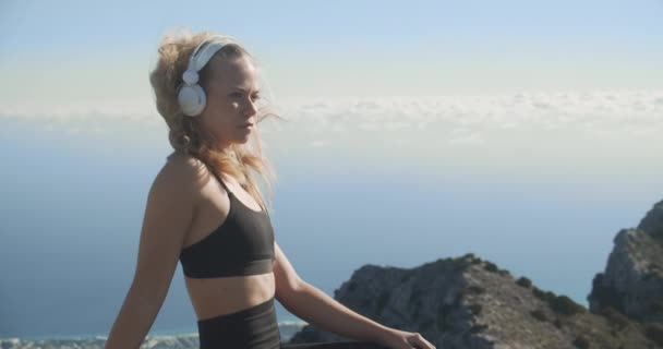 Mujer joven escuchando auriculares en la cima de la montaña — Vídeos de Stock