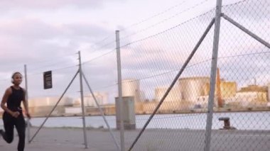 Spor Giyim ve Kulaklık Giyen Genç Kadın Liman boyunca koşuyor