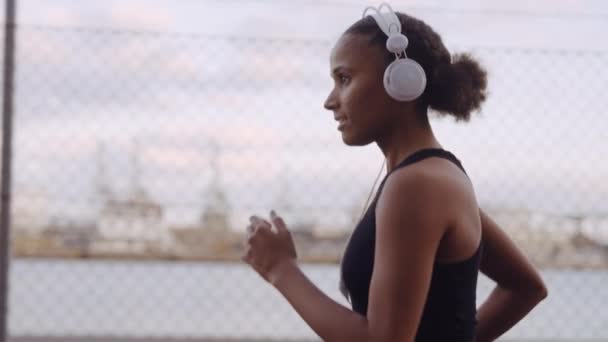 Mujer joven en ropa deportiva y auriculares corriendo a lo largo del puerto — Vídeos de Stock