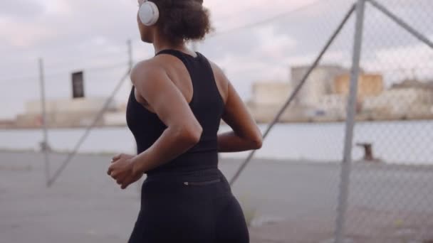 Junge Frau in Sportkleidung und Kopfhörer joggt am Hafen entlang — Stockvideo
