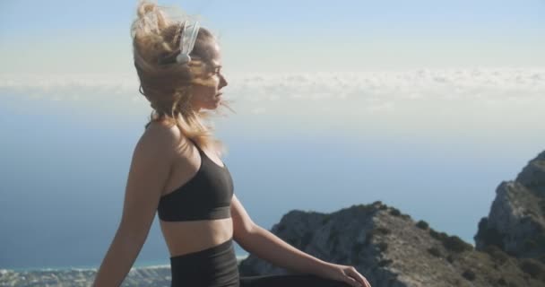 Mujer joven escuchando auriculares en la cima de la montaña — Vídeos de Stock