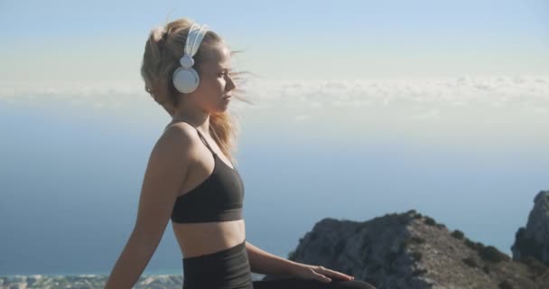 Mujer joven escuchando auriculares en la cima de la montaña — Vídeo de stock
