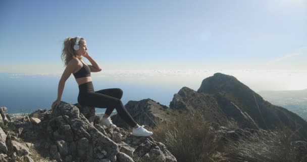 Mujer joven escuchando auriculares en la cima de la montaña — Vídeo de stock