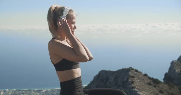 Mujer joven quitando auriculares en la cima de la montaña — Vídeo de stock