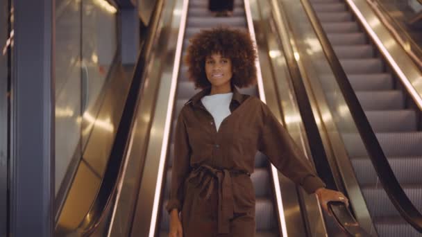 Młoda kobieta w brązowym z afro włosy schodzące z schodów ruchomych — Wideo stockowe
