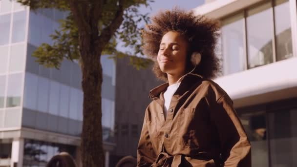 Mujer con afro perdido en la música de sus auriculares en la ciudad — Vídeos de Stock