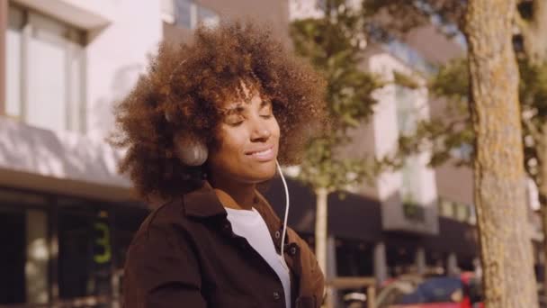 Женщина, любящая музыку из наушников в солнечном городе — стоковое видео