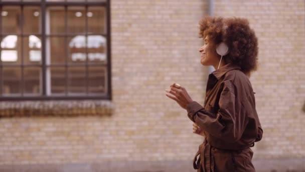 Mujer bailando con música a través de auriculares mientras se mueve por la calle — Vídeos de Stock