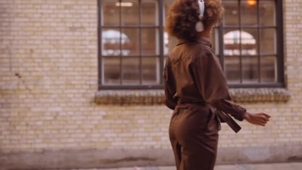 Kvinna dansar till musik genom hörlurar när hon rör sig nerför gatan — Stockvideo