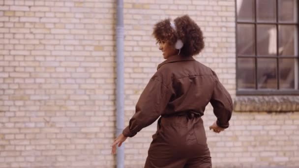 Танцующая женщина смеется, слушая музыку через наушники на улице — стоковое видео
