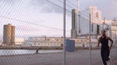 Spor Giyim ve Kulaklık Giyen Genç Kadın Liman boyunca koşuyor