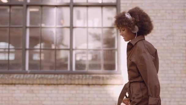 Жінка танцює коли вона рухається вулицею до музики через навушники — стокове відео
