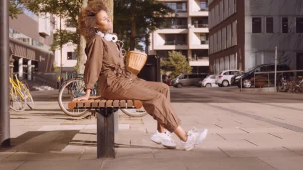 Kvinnan i Brown Jumpsuit sitter på Sunny City Bench — Stockvideo