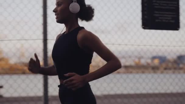 Jonge vrouw in sportkleding en koptelefoon loopt langs de haven — Stockvideo