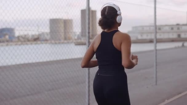 Mujer joven en ropa deportiva negra trotando a lo largo del puerto — Vídeos de Stock