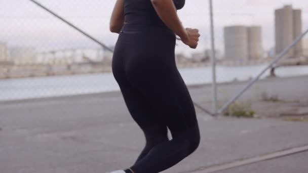 Νεαρή γυναίκα με μαύρα αθλητικά τζόκινγκ κατά μήκος του λιμανιού — Αρχείο Βίντεο