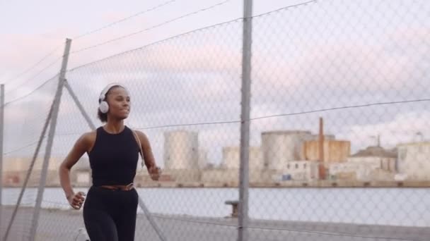 Молодая женщина в спортивной одежде и наушниках бегает по гавани — стоковое видео