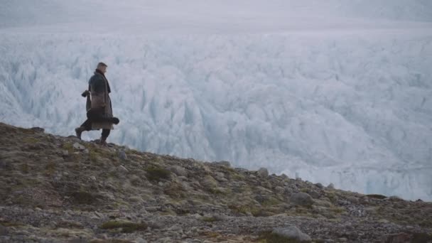 Man met gitaarkoffer en grote jas wandelen langs Ridge door gletsjer — Stockvideo