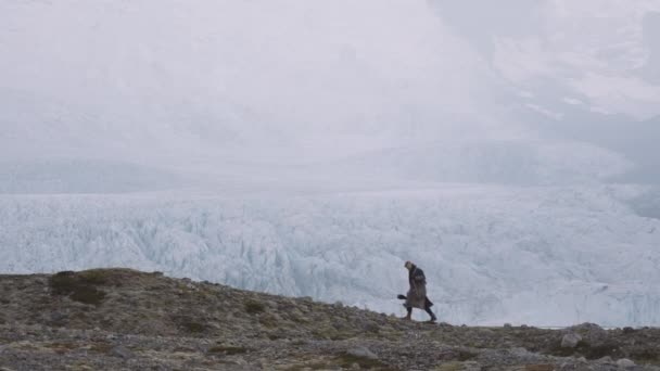 Muž s pouzdrem na kytaru a velkým pláštěm kráčející podél hřebene po ledovci — Stock video