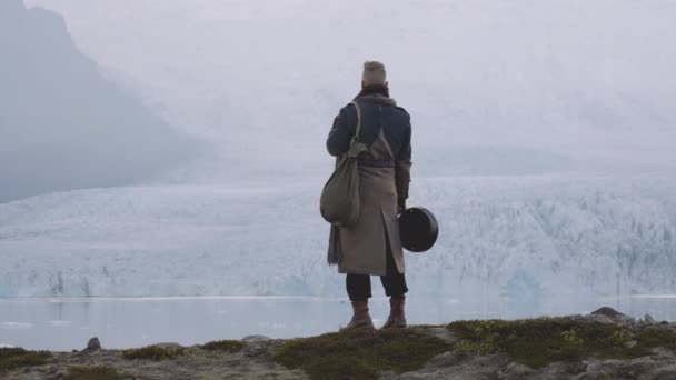 Man med gitarr fall och stor rock står på åsen av Glacier — Stockvideo