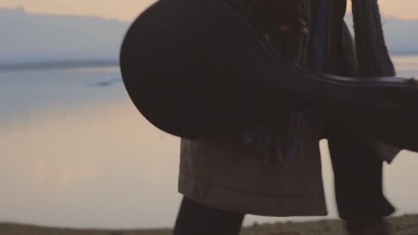 Hombre que lleva el estuche de la guitarra a través del paisaje frío del atardecer — Vídeo de stock