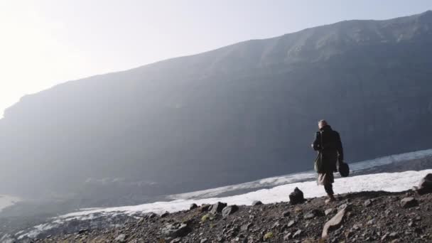 Homme qui voyage en descendant une colline rocheuse près d'un glacier — Video
