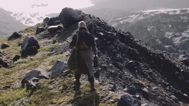 Man In Greatcoat Walking Along Rocky Ridge Towards Sunlit Valley — Stock video