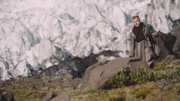 Man in grote jas dragen gitaar geval en tas weg van gletsjer — Stockvideo