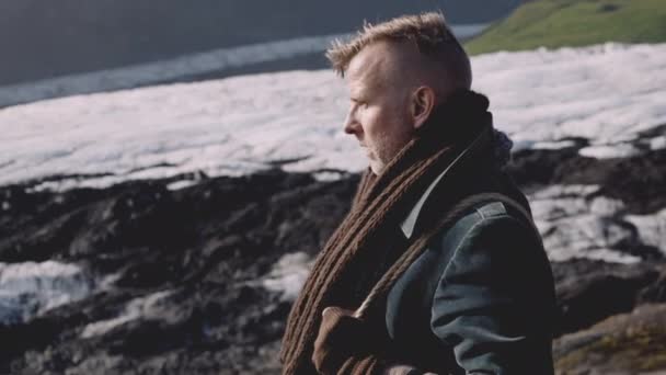 Uomo che cammina in sciarpa e cappotto attraverso paesaggio roccioso con ghiacciaio — Video Stock