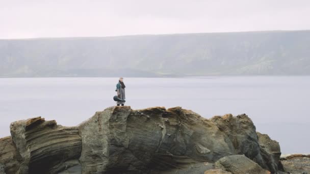 Man met gitaarkoffer staand op rots in IJslands landschap — Stockvideo