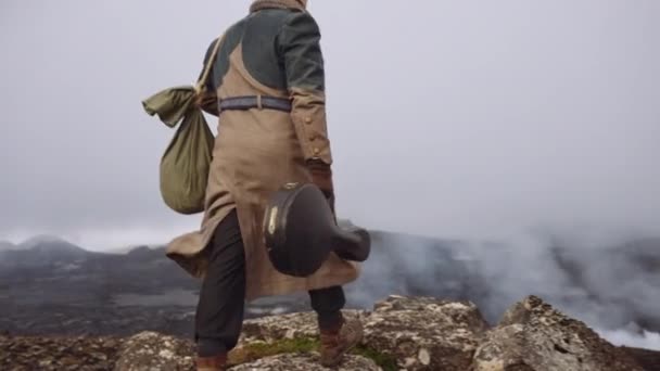 Hombre viajero llevando estuche de guitarra y caminando hacia rocas brumosas — Vídeos de Stock