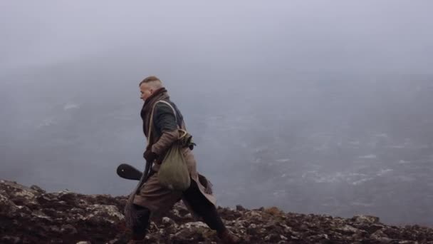 Reizende man draagt gitaar geval en lopen over mistige rotsen — Stockvideo