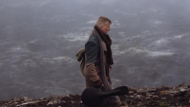 Reisender Mann trägt Gitarrenkoffer, der über neblige Felsen läuft — Stockvideo