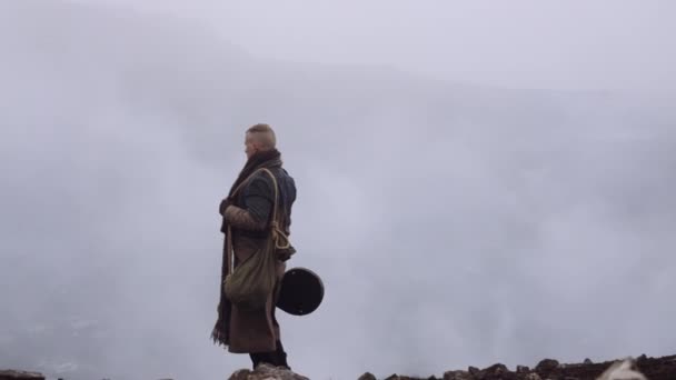 Homem de casaco grande em pé na paisagem nebulosa e rochosa — Vídeo de Stock