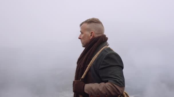 Людина в чорному пальто стоїть у туманному і скелястому ландшафті — стокове відео