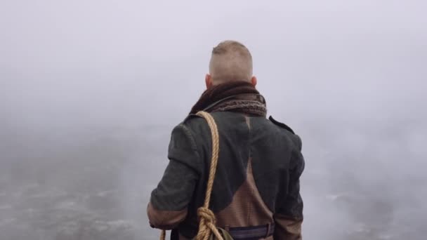 Homem de casaco grande em pé na paisagem nebulosa e rochosa — Vídeo de Stock