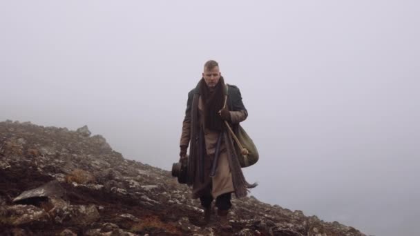 Man i stor rock vandrar genom dimmiga och bergiga landskap — Stockvideo