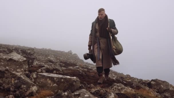 Człowiek w wielkim płaszczu przechadza się po mglistym i skalistym krajobrazie — Wideo stockowe
