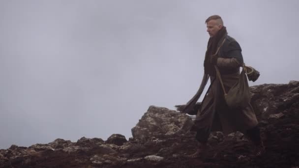 Людина в масляному плащі йде крізь туманний і скелястий ландшафт — стокове відео