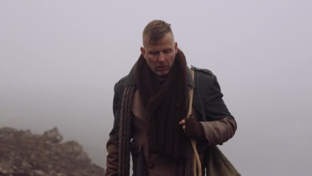 Человек в большом пальто прогуливается по туманному и скалистому ландшафту — стоковое видео