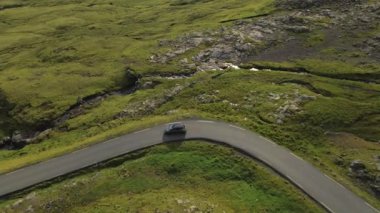 Faroe Adası 'nın dramatik kırsalında dolambaçlı yol boyunca araba süren insansız hava aracı.